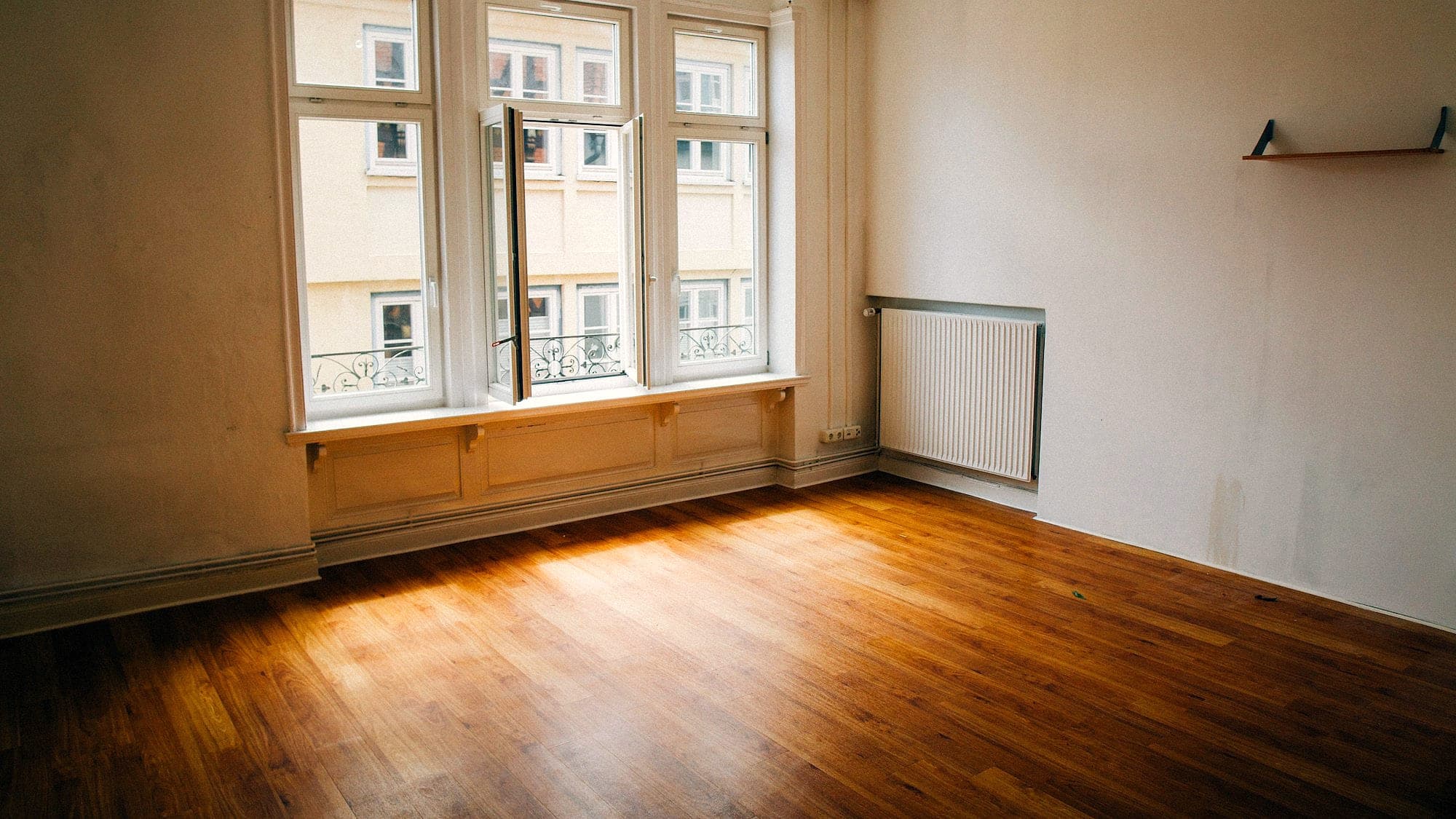 Leere helle Wohnung mit Parkettboden und hohen Fenstern, zwischen zwei Mietverhältnissen.