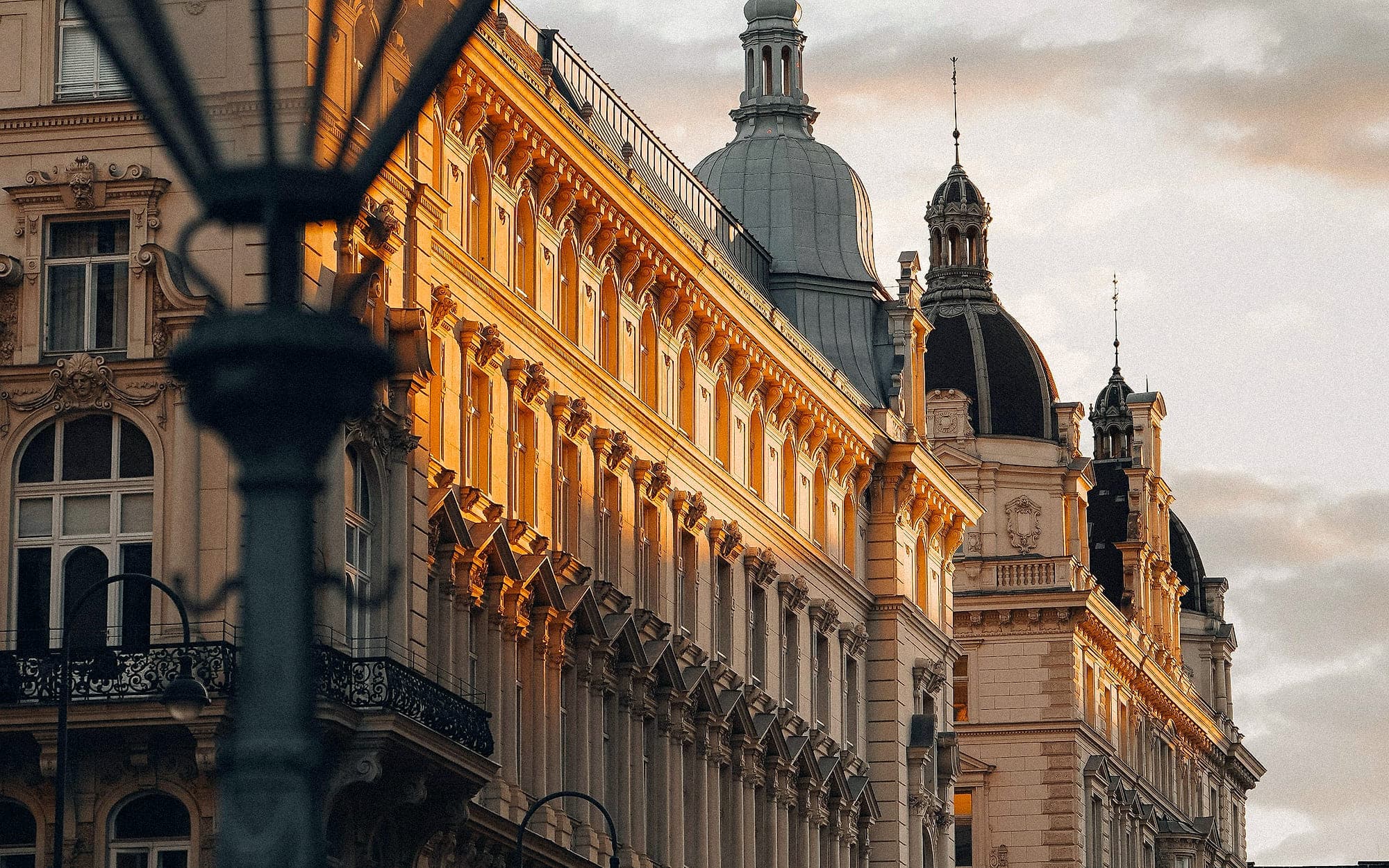 Wiener Altbaufassaden im Abendlicht, Fensterreihen und Kuppeln, im Vordergrund eine Straßenlaterne.